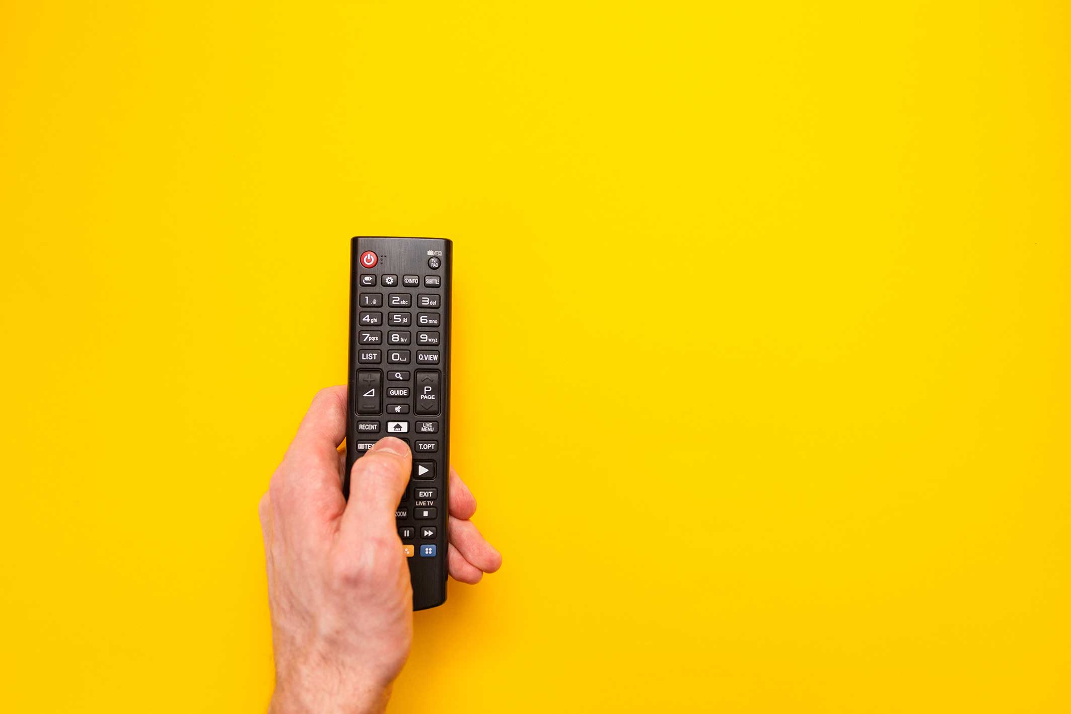 Person pressing a button on a tv remote control on a plain yellow background