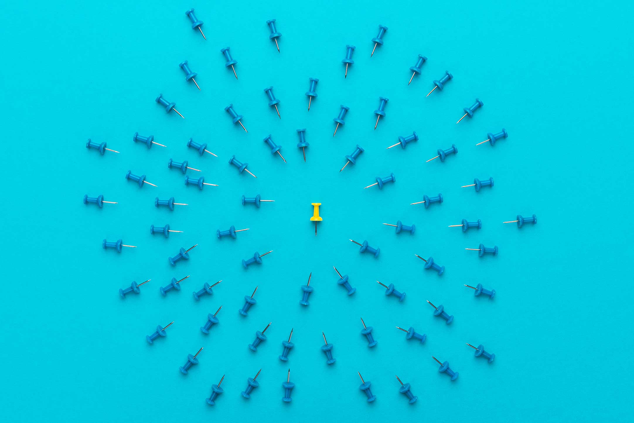 yellow push pin surrounded by blue push pins on a plain blue background